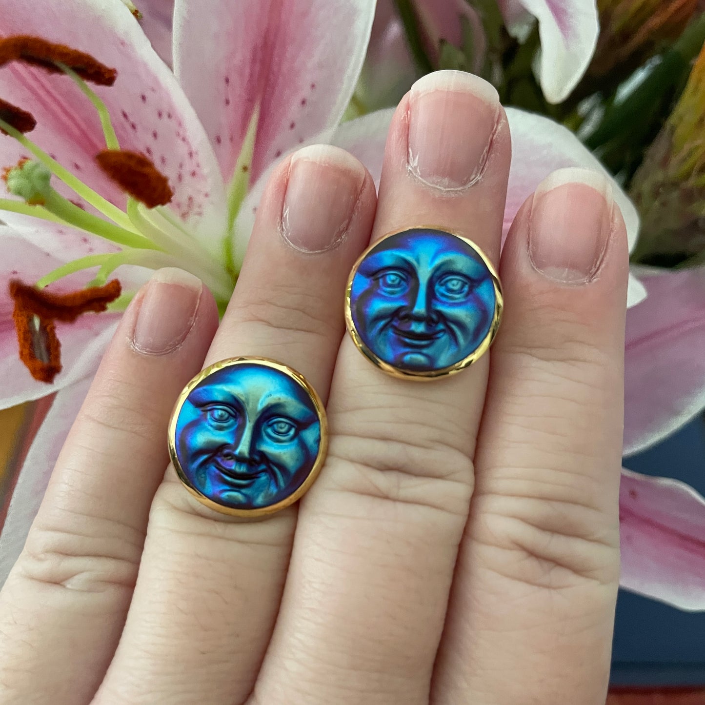 Hand wearing 2 button rings with blue colored face design against a floral background