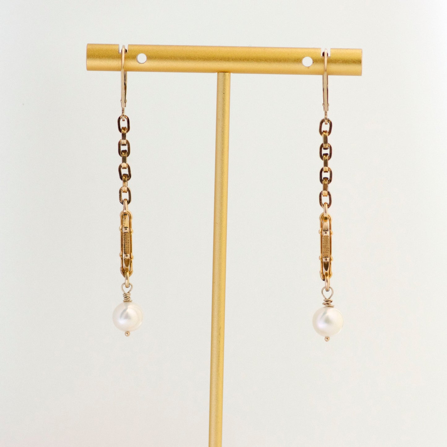 Long Dangling Pearl Drop Antique Watch Chain Earrings hanging on gold tone earring T stand.