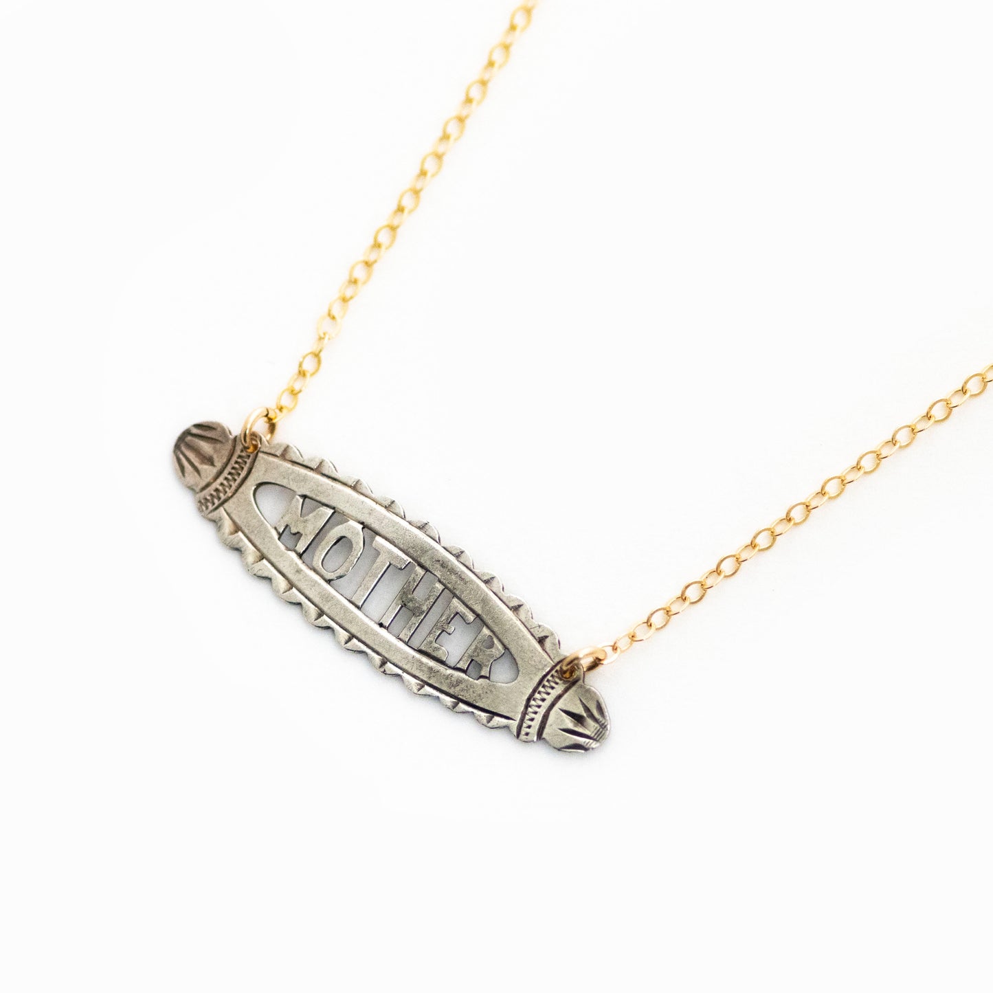 This antique conversion necklace is made up of: Sterling silver Victorian bar pin pendant from the late 1800s with hand fabricated details depicting the word "MOTHER". Arranged at an angle from a 14k gold filled cable chain that extends toward the top right corner..