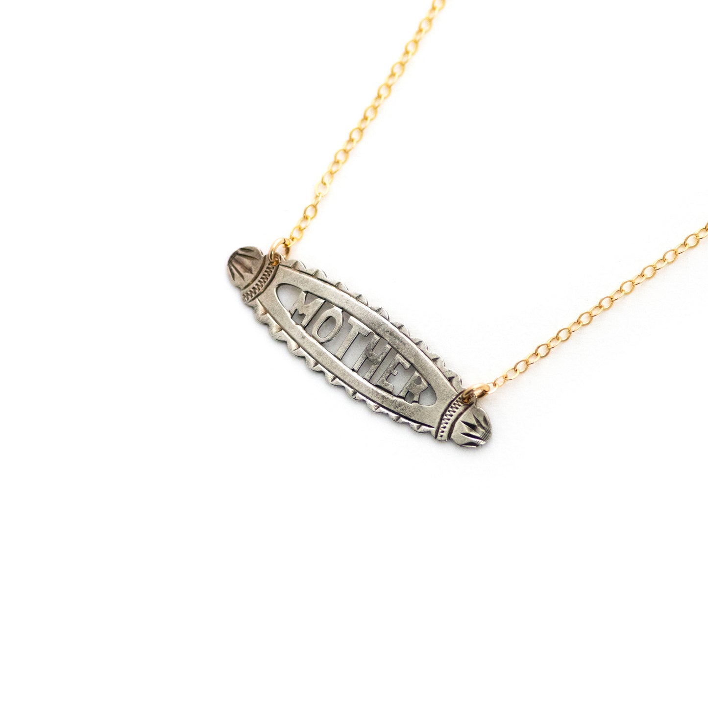 This antique conversion necklace is made up of: Sterling silver Victorian bar pin pendant from the late 1800s with hand fabricated details depicting the word "MOTHER". Arranged at an angle from a 14k gold filled cable chain that extends toward the top right corner..