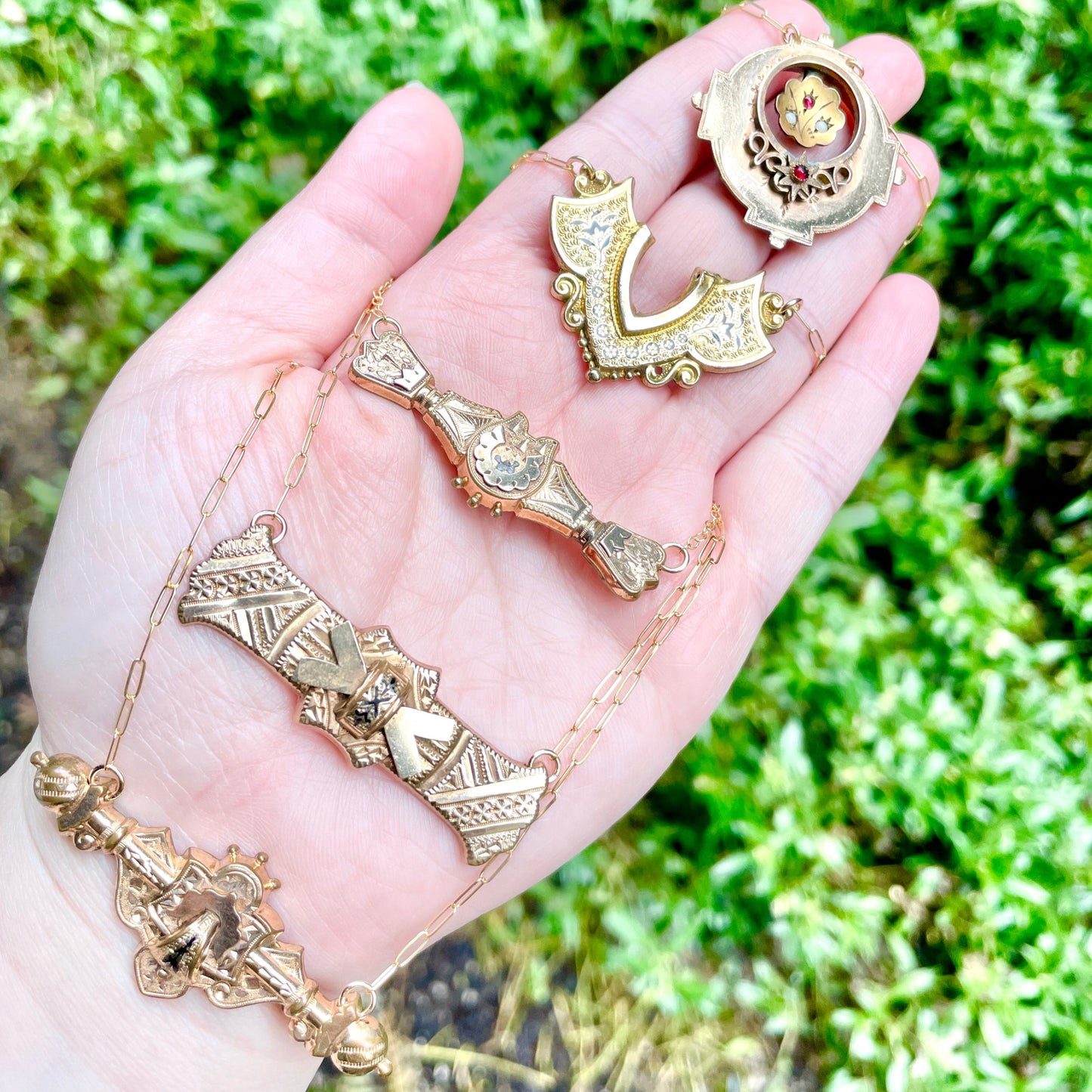 5 brooch and bar pin conversion necklaces laying on palm side of hand with green natural background