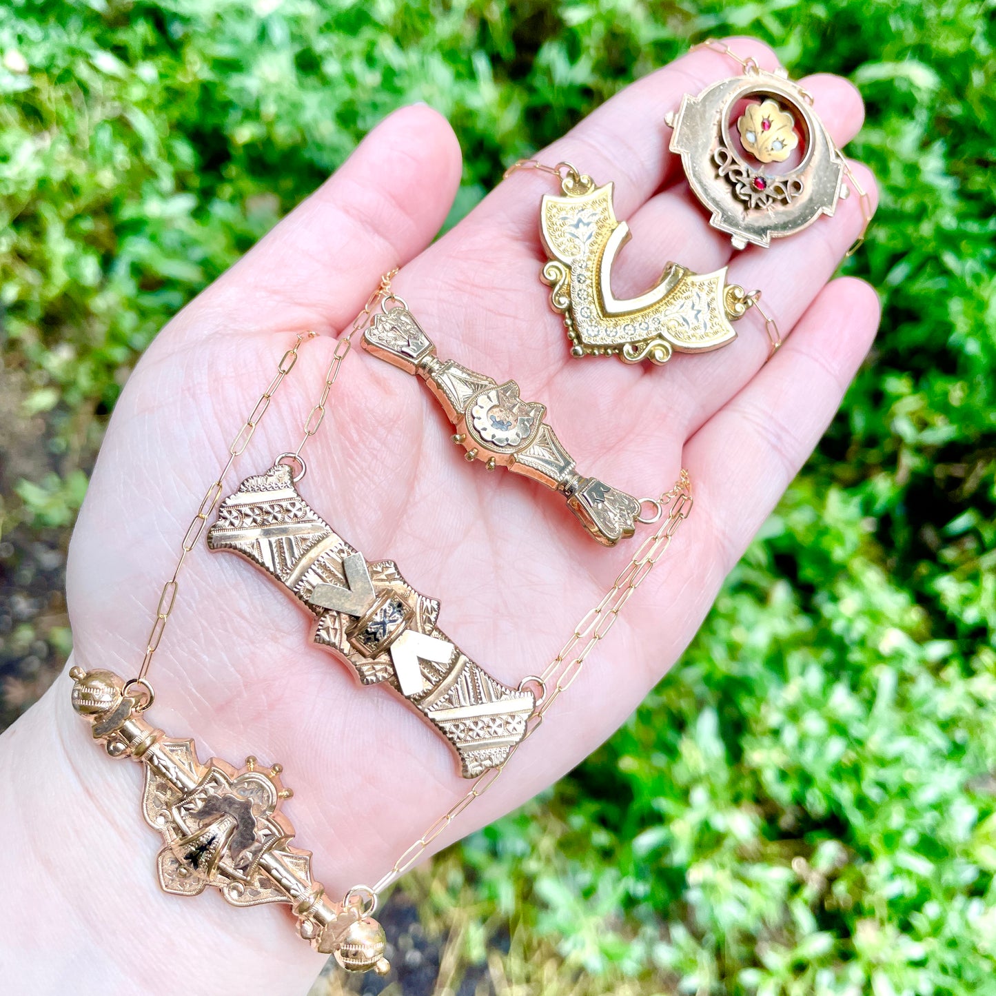 Five brooch and bar pin conversion necklaces laying on palm side of hand with green natural background