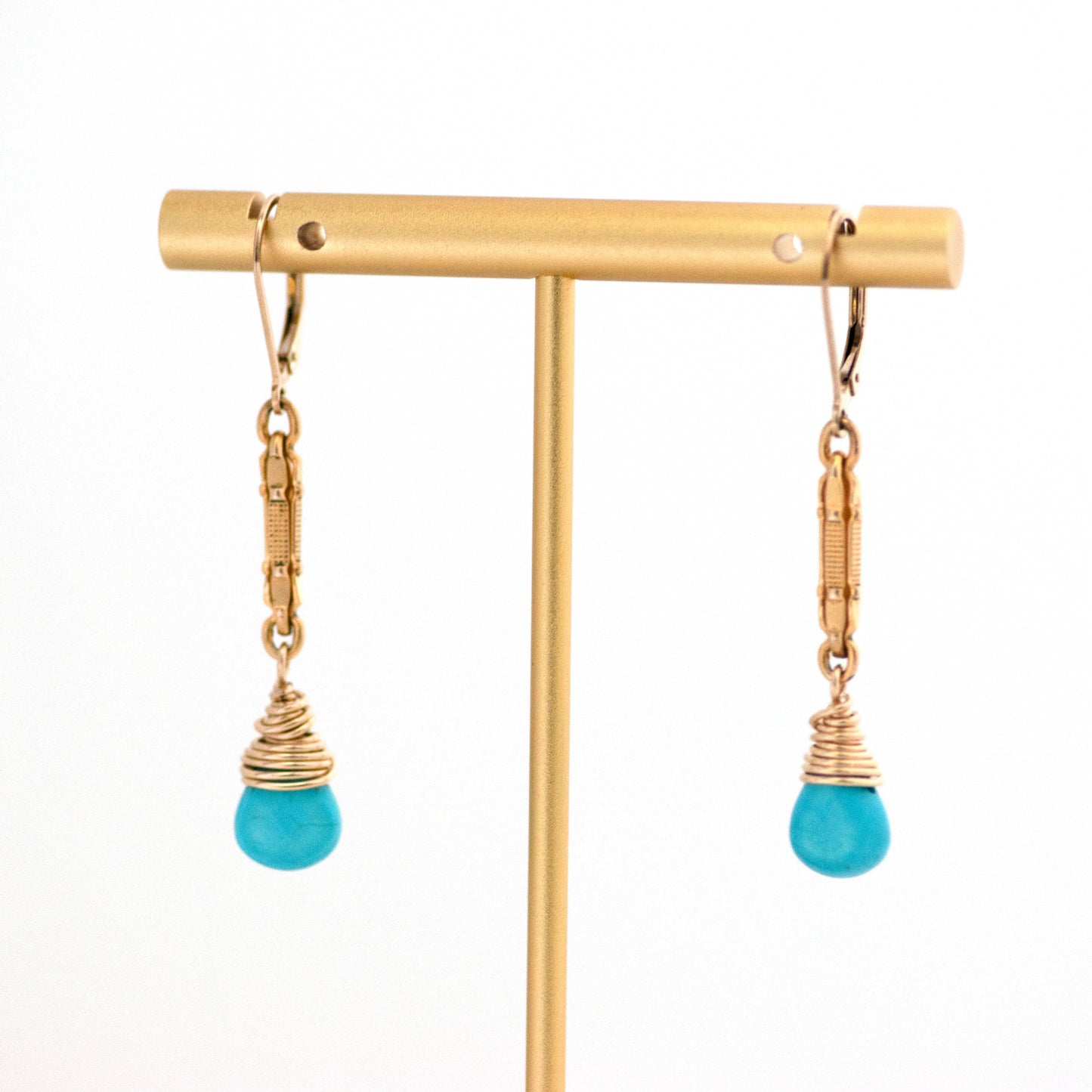 These one-of-a-kind conversion earrings are made up of:  Gold filled antique Victorian watch chain links from the late 1800s with hand tooled details and wire wrapped Arizona turquoise briolettes. Earrings are hanging from a gold T bar earrings stand display.