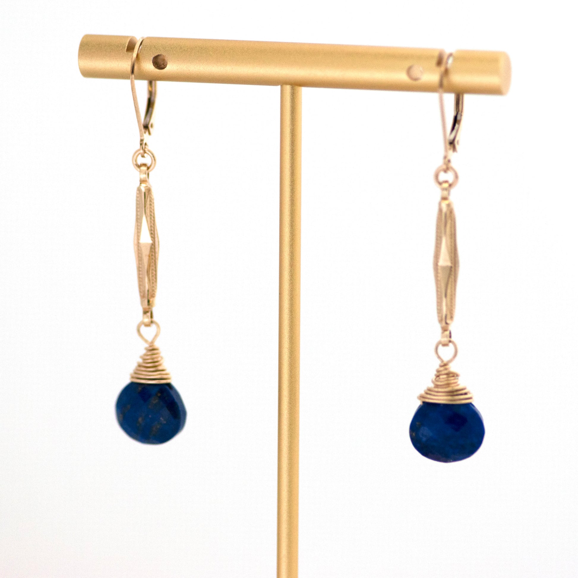 These one-of-a-kind conversion earrings are made up of:  Gold filled antique Edwardian watch chain links from the early 1900s with hand tooled details. Lapis lazuli. Earrings hanging from T bar earring stand.