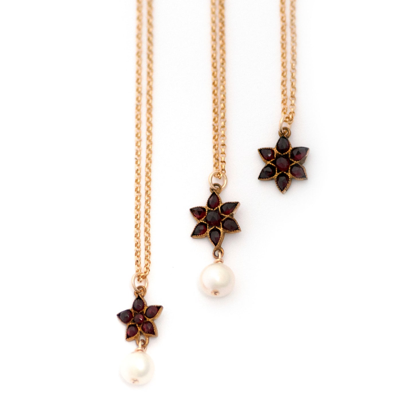 Three necklaces, each with star pendants filled with Bohemian Garnets. Two of the necklaces have a wire wrapped freshwater pearl dangling from the star pendant.
