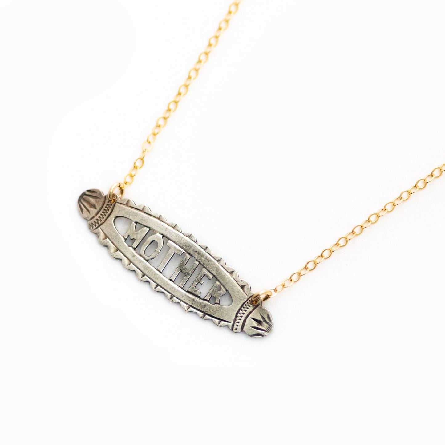 This antique conversion necklace is made up of:  Sterling silver Victorian bar pin pendant from the late 1800s with hand fabricated details depicting the word "MOTHER". Arranged at an angle from a 14k gold filled cable chain that extends toward the top right corner..