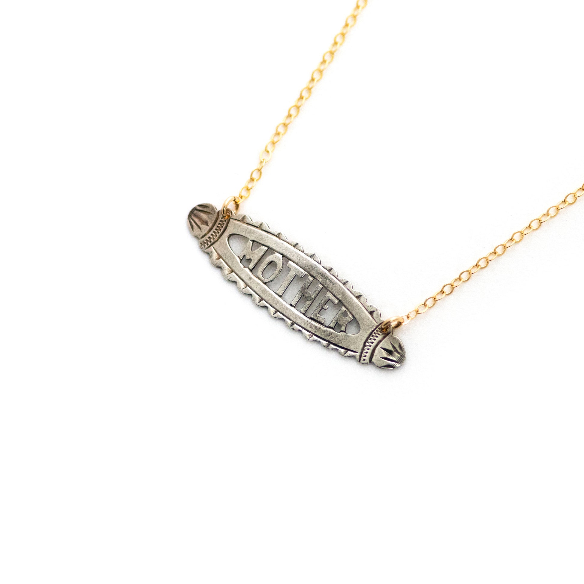 This antique conversion necklace is made up of:  Sterling silver Victorian bar pin pendant from the late 1800s with hand fabricated details depicting the word "MOTHER". Arranged at an angle from a 14k gold filled cable chain that extends toward the top right corner..