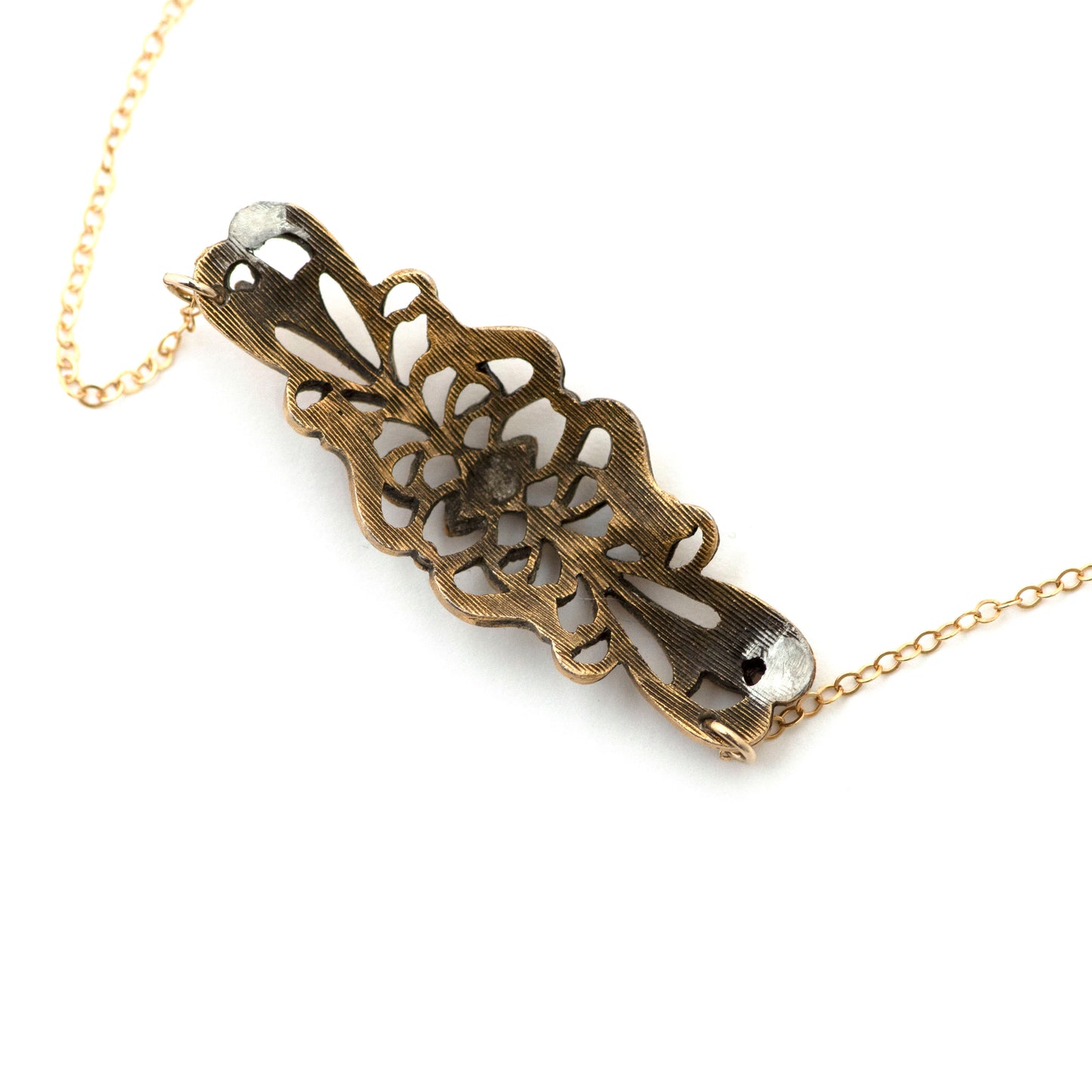 A product photography image of the backside of a vintage bar pin repurposed pendant dangling on a 14k gold filled cable chain on a white background. 