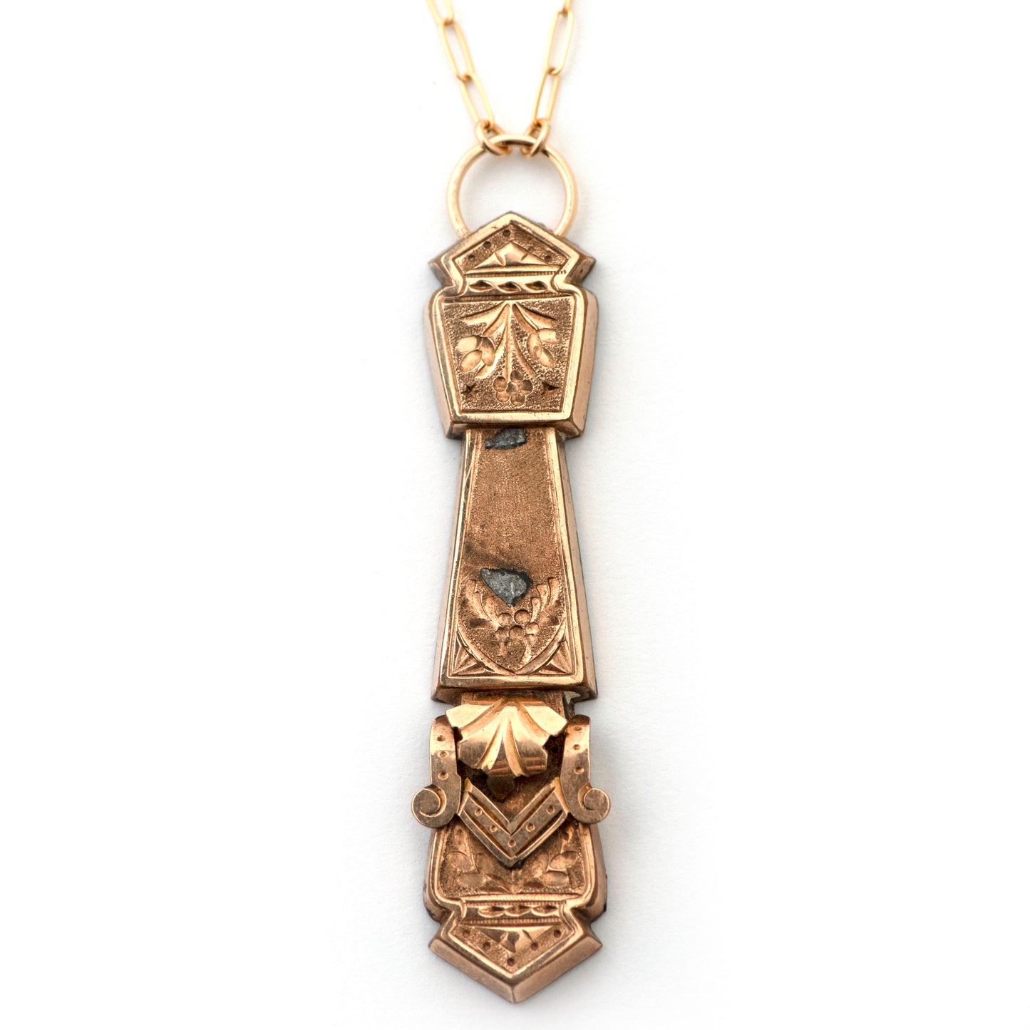 An antique bar pin conversion to vertical pendant shown on an all white background. Pendant resembles a thick sword shape or column/pillar shape, has hand engraved details and other 3 dimensional gold filled details.