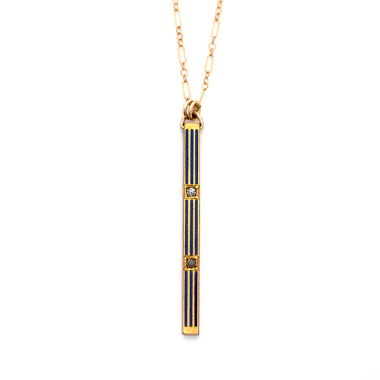 An antique Gold washed Art Deco bar pin pendant from the 1920s with deep blue enamel and clear paste rhinestones strung on an gold filled chain and lying on an all white background.