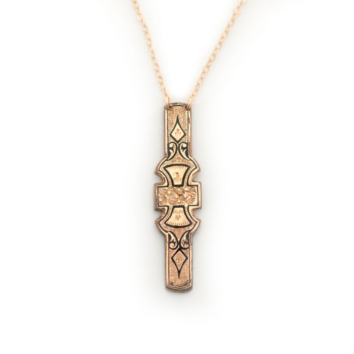 An antique vertical bar pin conversion pendant necklace on an all white background. Pendant is gold filled and decorated with black enamel tracery, also known as taille d'epargne.