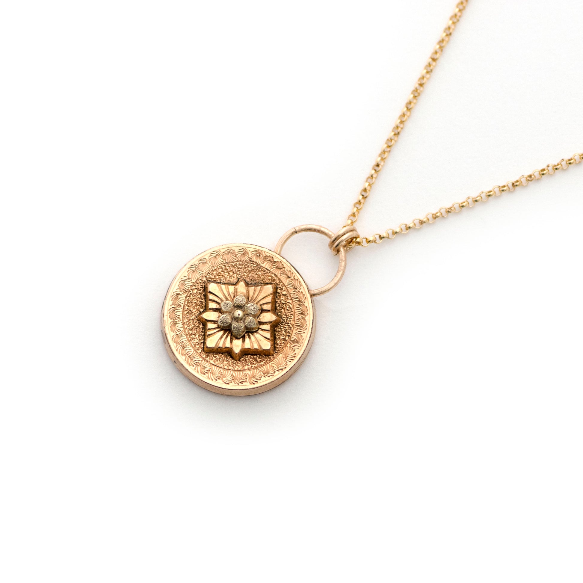 An antique cufflink conversion pendant resembling a door knocker shape that is strung on a 14k gold filled chain and laying on an all white background.