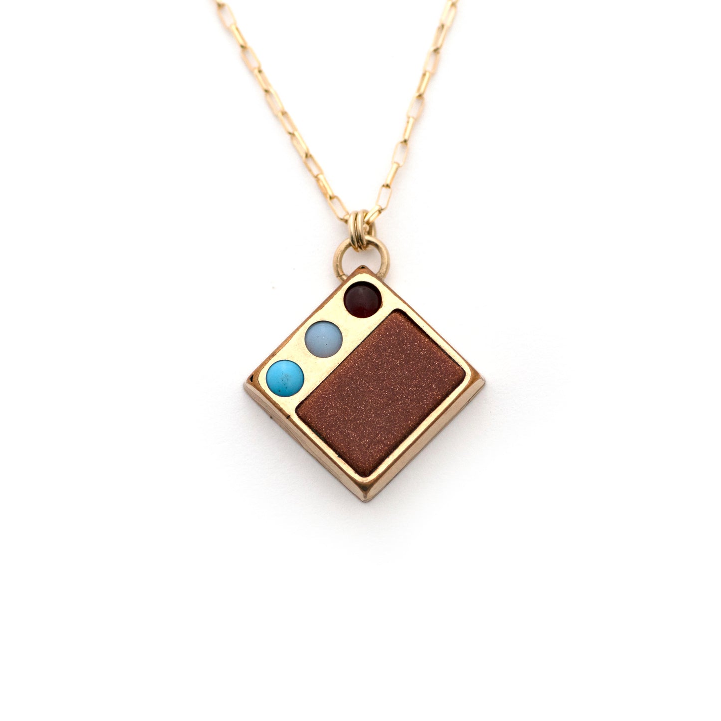 An antique gold filled Victorian cufflink conversion pendant with goldstone as well as red, white, and blue glass details. Cufflink conversion pendant necklace is laying on an all white background.