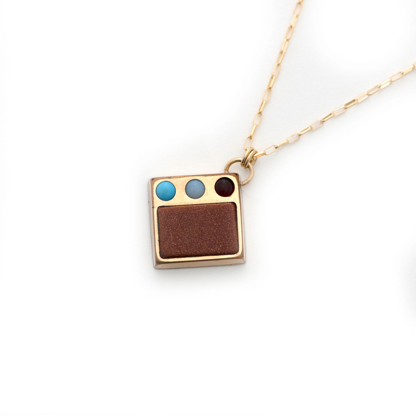 An antique gold filled Victorian cufflink conversion pendant with goldstone as well as red, white, and blue glass details. Cufflink conversion pendant necklace is laying on an all white background.