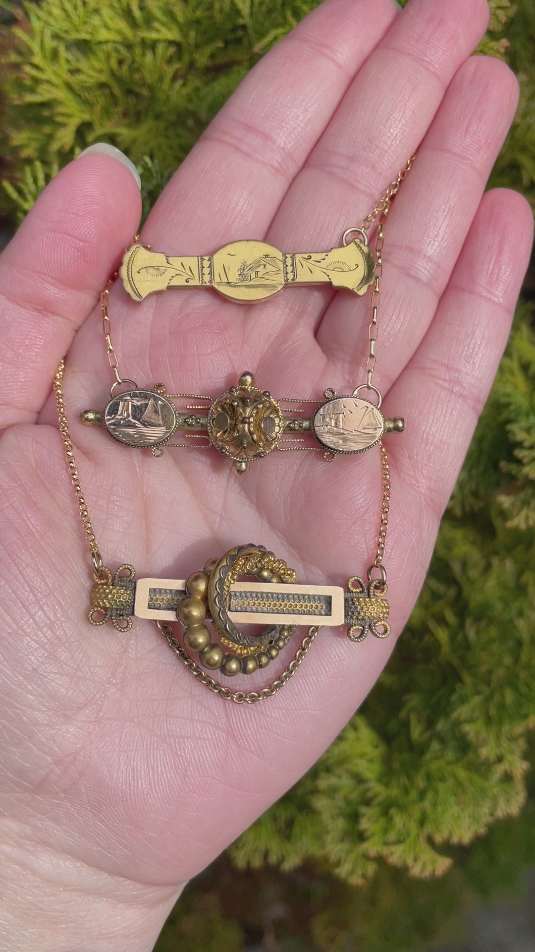 video of three antique victorian bar pin necklaces displayed on the palm of a hand with a background of evergreen foliage