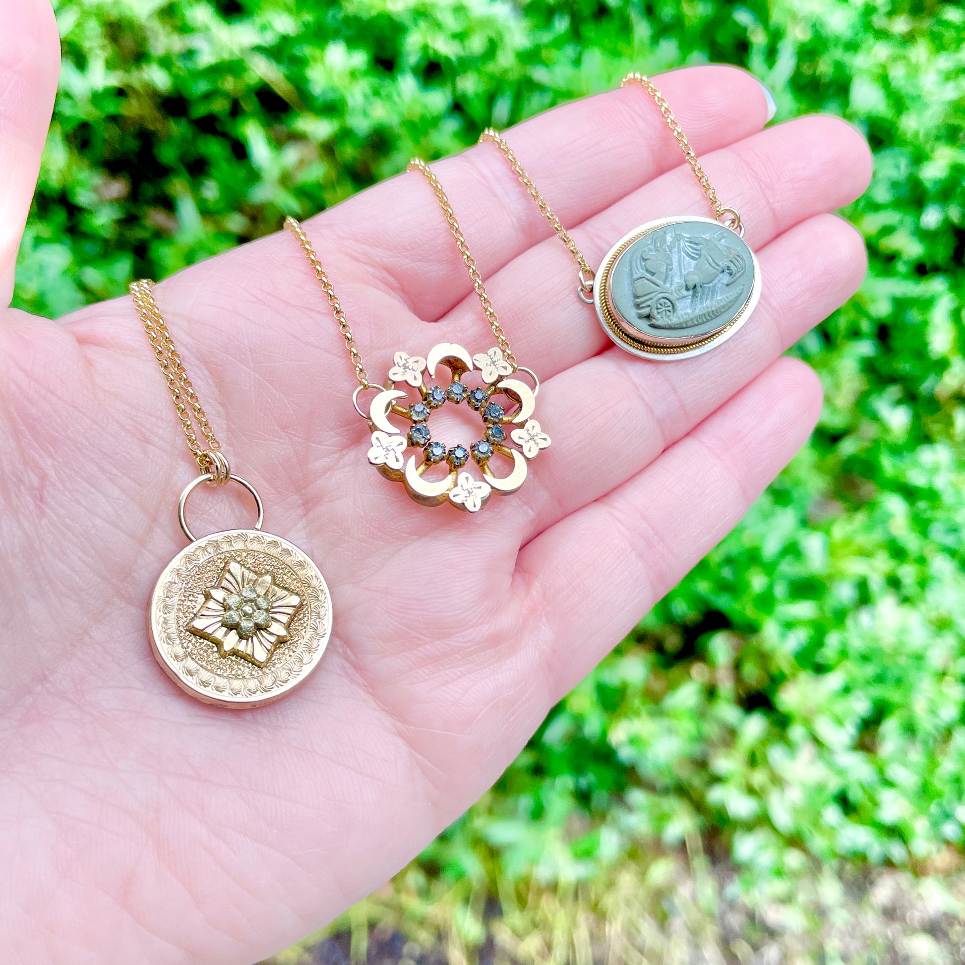 Three antique conversion pendant necklaces laying on the palm side of a left hand with green foliage in the background.