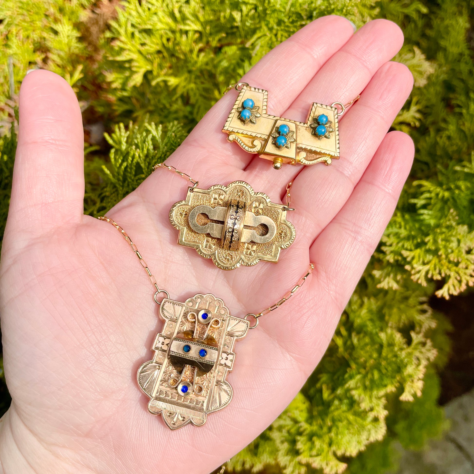 Three goregous and statement making antique Victorian brooch conversion necklaces in the palm of a hand against an evergreen background