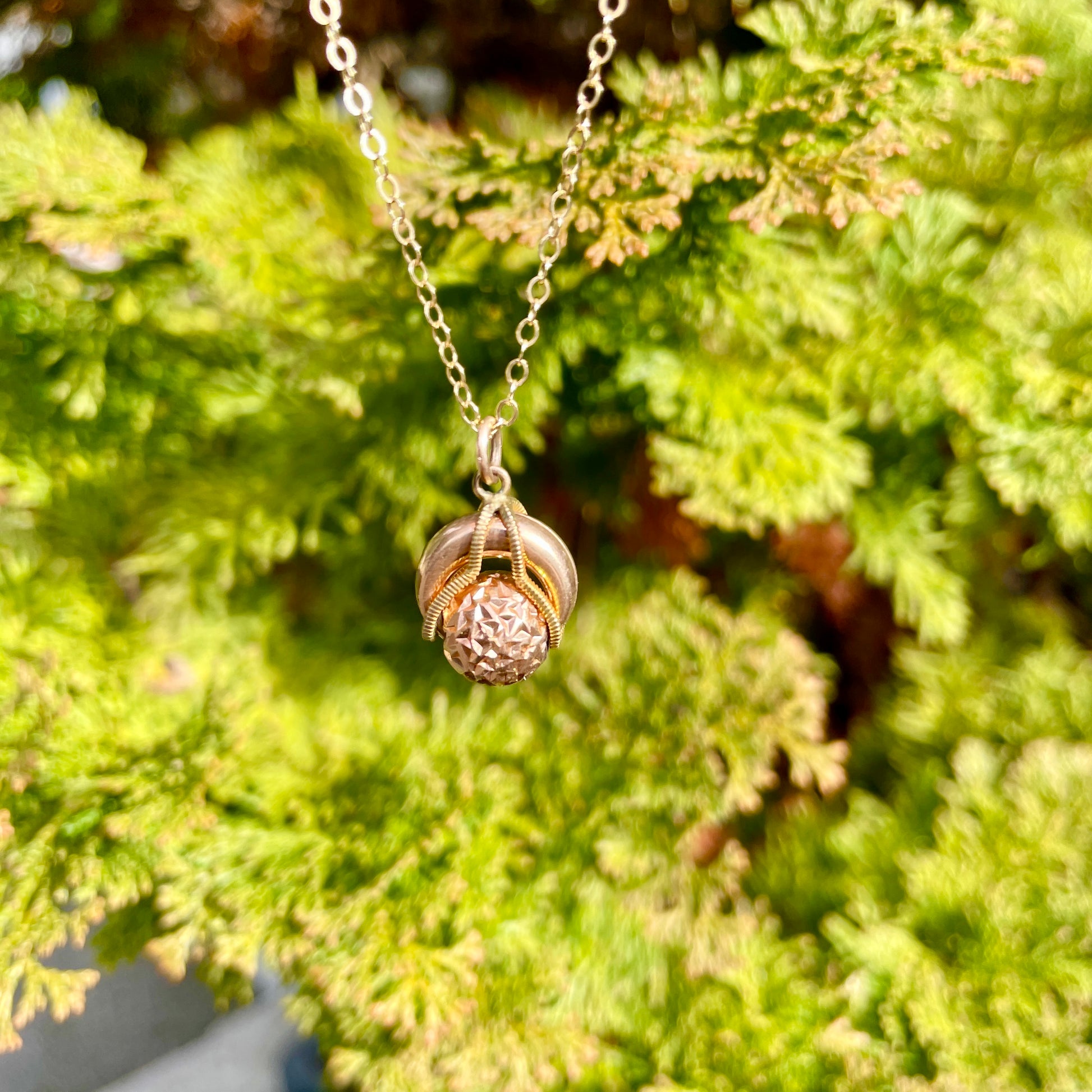 steampunk victorian antique rolling ball gold filled pendant necklace hanging in front of a back ground of green foliage