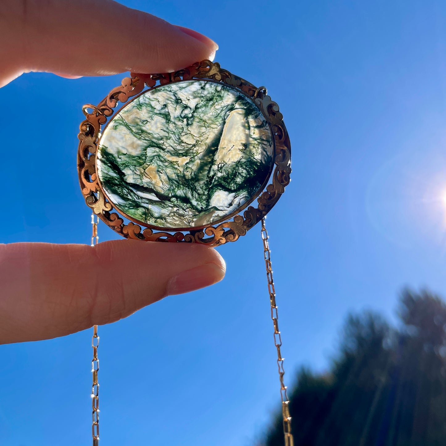 Antique Victorian Crystal Quartz Moss Green Agate Necklace held up to the blue sky and sunlight passing through the stone